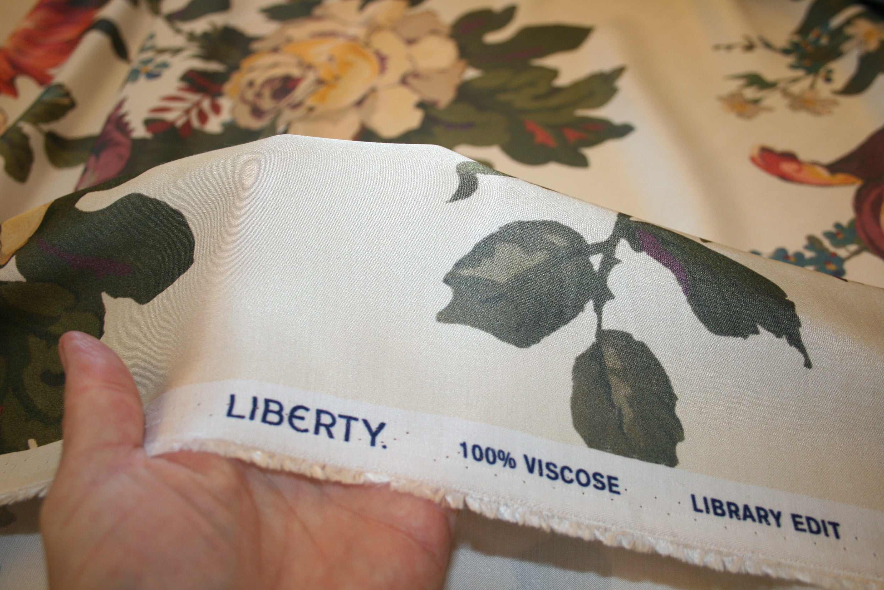 Let satinvævet viskose fra Liberty med blomsterprint i varme nuancer på lys champagne bund
