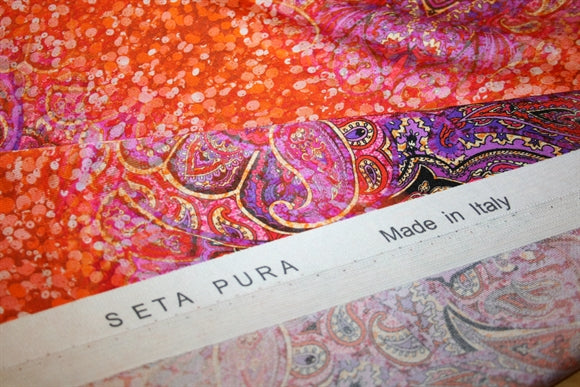 Detalje af 'Ardente' silkestof –
dekorative borter og paisleymotiver
i varme orange og lilla toner
